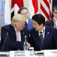 U.S. President Donald Trump and then-Prime Minister Shinzo Abe shake hands alongside Chinese President Xi Jinping after a special event at the Group of 20 summit in Osaka on June 28, 2019. | KYODO