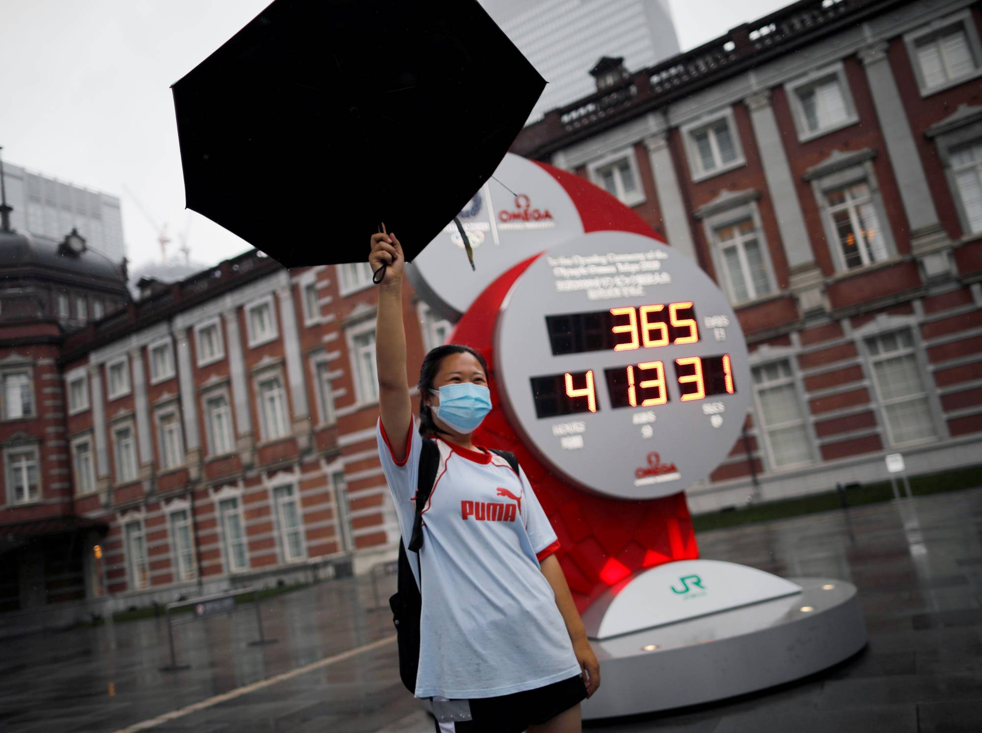 A woman poses for a photo in front of a countdown clock for the postponed Tokyo 2020 Olympic Games outside Tokyo station in July.  | REUTERS