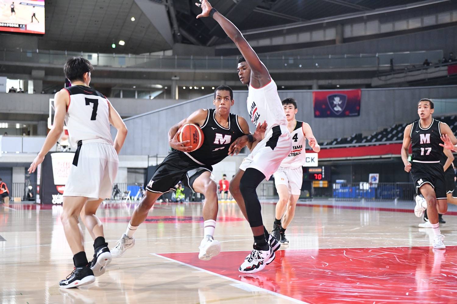 Meisei's Ibu Yamazaki (second from left) attacks the basket while being defended by Higashiyama center Jean Pierre Mutombo on Tuesday at Tokyo Metropolitan Gymnasium. | Courtesy of the Japan Basketball Association 