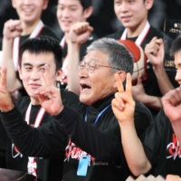 Meisei head Hisao Sato (center) celebrates with his players after Tuesday\'s win at Tokyo Metropolitan Gymnasium. | COURTESY OF THE JAPAN BASKETBALL ASSOCIATION