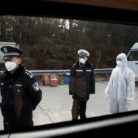 A medical worker and police wait for drivers at a checkpoint in Yunxi county, in China\'s Hunan province, near the border to Hubei province, amid lockdowns in January. 
 | REUTERS 