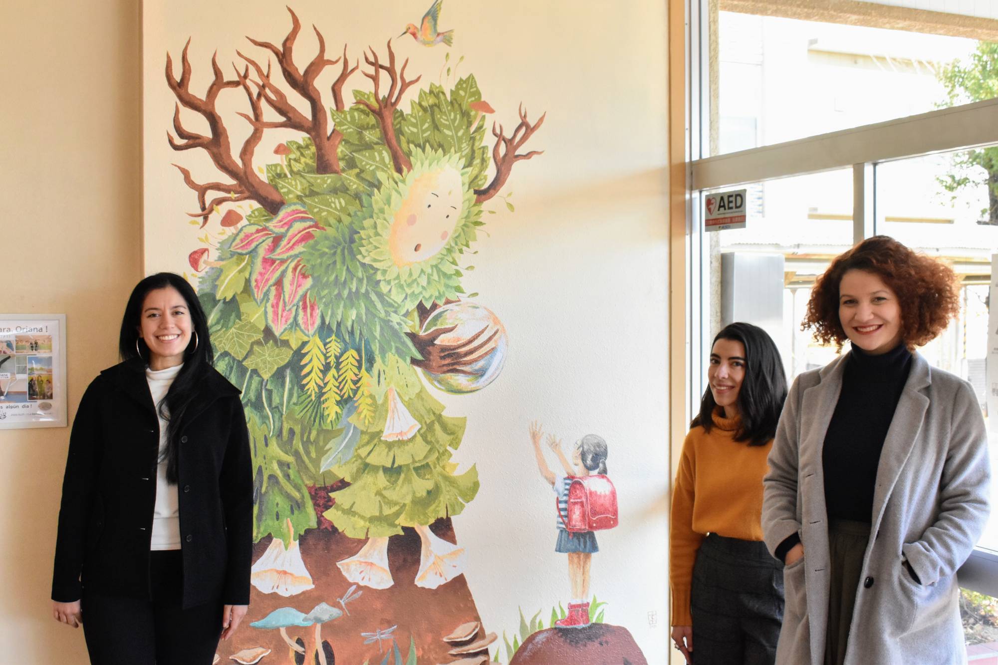 Teresa Currea (left), Oriana Marin (center) and Clara Campos (right) pose in front of a painting that represents the concept of Mother Nature and friendship. | TOMOHIRO OSAKI 