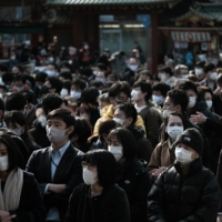 People wearing protective face masks as they line up to offer prayers on the first business day of the year at the Kanda Myojin shrine in Tokyo on Monday. | BLOOMBERG