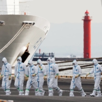 Workers wear protective gear to protect them against the COVID-19 virus near the cruise ship Diamond Princess at Daikoku Pier Cruise Terminal in Yokohama last February. More than 700 of the 3,711 people on board the ship became infected with the virus, with 14 deaths being reported. |  REUTERS