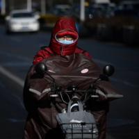 A man wrapped up in the cold rides his motorcycle along a street on a winter day in Beijing on Thursday, after China\'s meteorological authority recently issued a severe weather warning across large parts of the country.  | AFP-JIJI