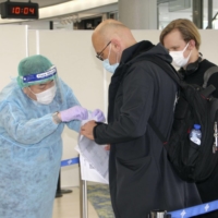 A staff member at Narita Airport near Tokyo speaks to passengers from Europe on Dec. 28. | KYODO