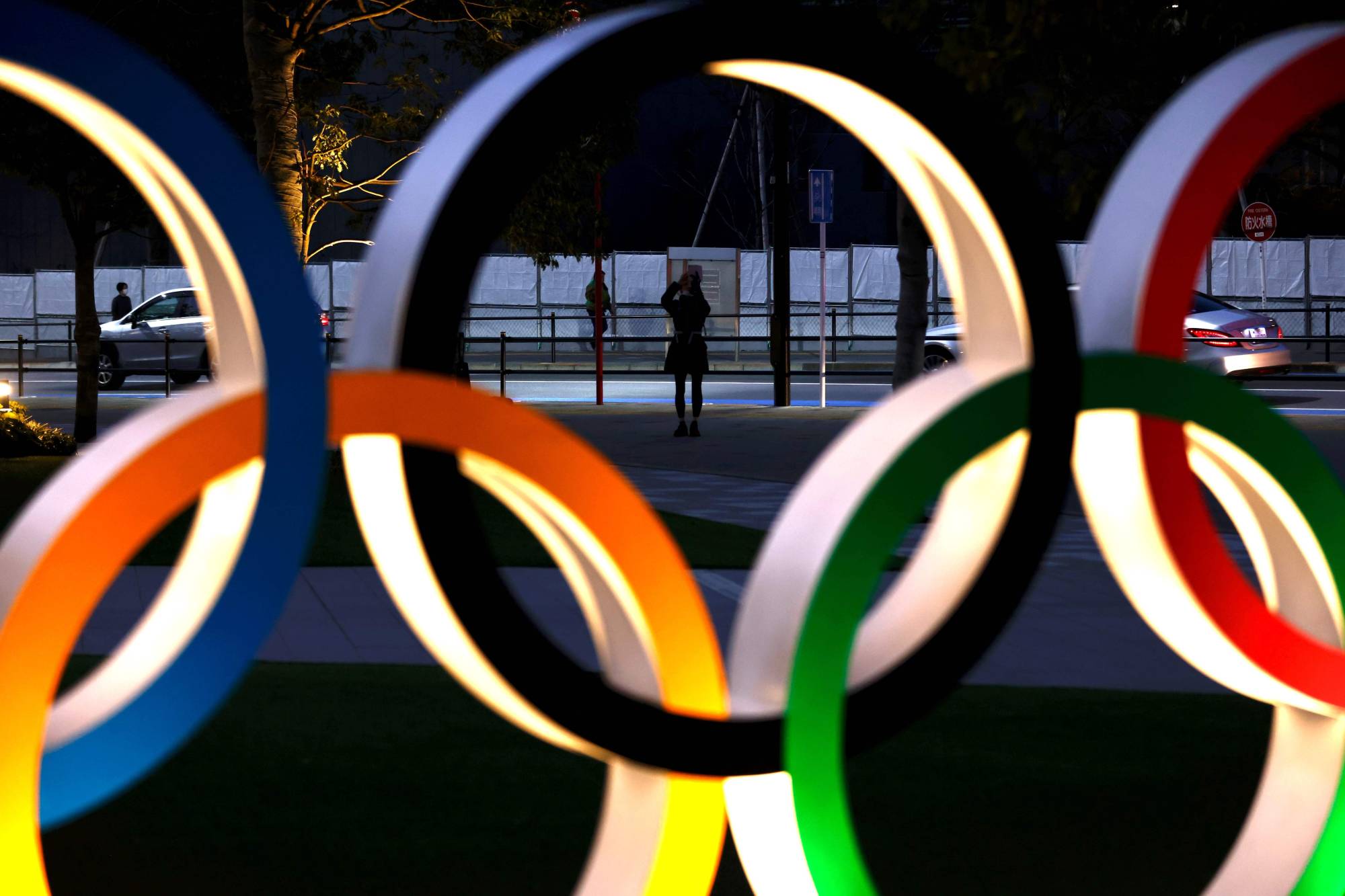 A woman takes pictures of Olympic rings in Tokyo on Friday. In a new poll, 35.3% of people in Japan called for the cancellation of the Tokyo Games, while 44.8% said the event should be put off again. | AFP-JIJI