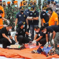 Rescue workers inspect recovered items and debris at the port in Jakarta on Sunday during the search operation for Sriwijaya Air flight SJ182, which crashed after takeoff from Jakarta on Saturday. | AFP-JIJI
