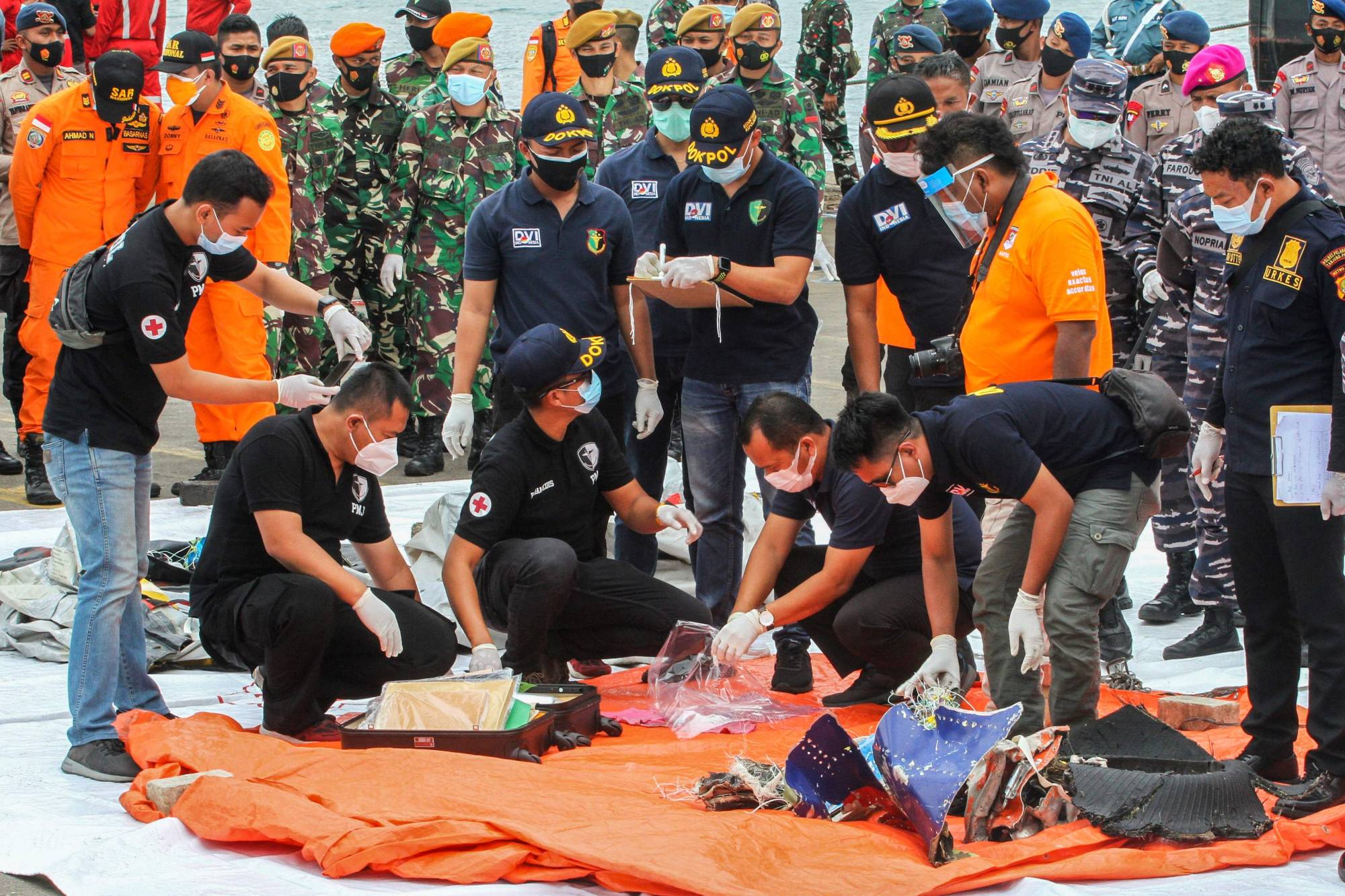 Rescue workers inspect recovered items and debris at the port in Jakarta on Sunday during the search operation for Sriwijaya Air flight SJ182, which crashed after takeoff from Jakarta on Saturday. | AFP-JIJI