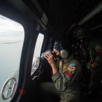 An Indonesian Air Force member looks through the window of a helicopter during an aerial search for the Sriwijaya Air SJ182, which crashed into the sea near Jakarta, on Sunday. | ANTARA FOTO / VIA REUTERS