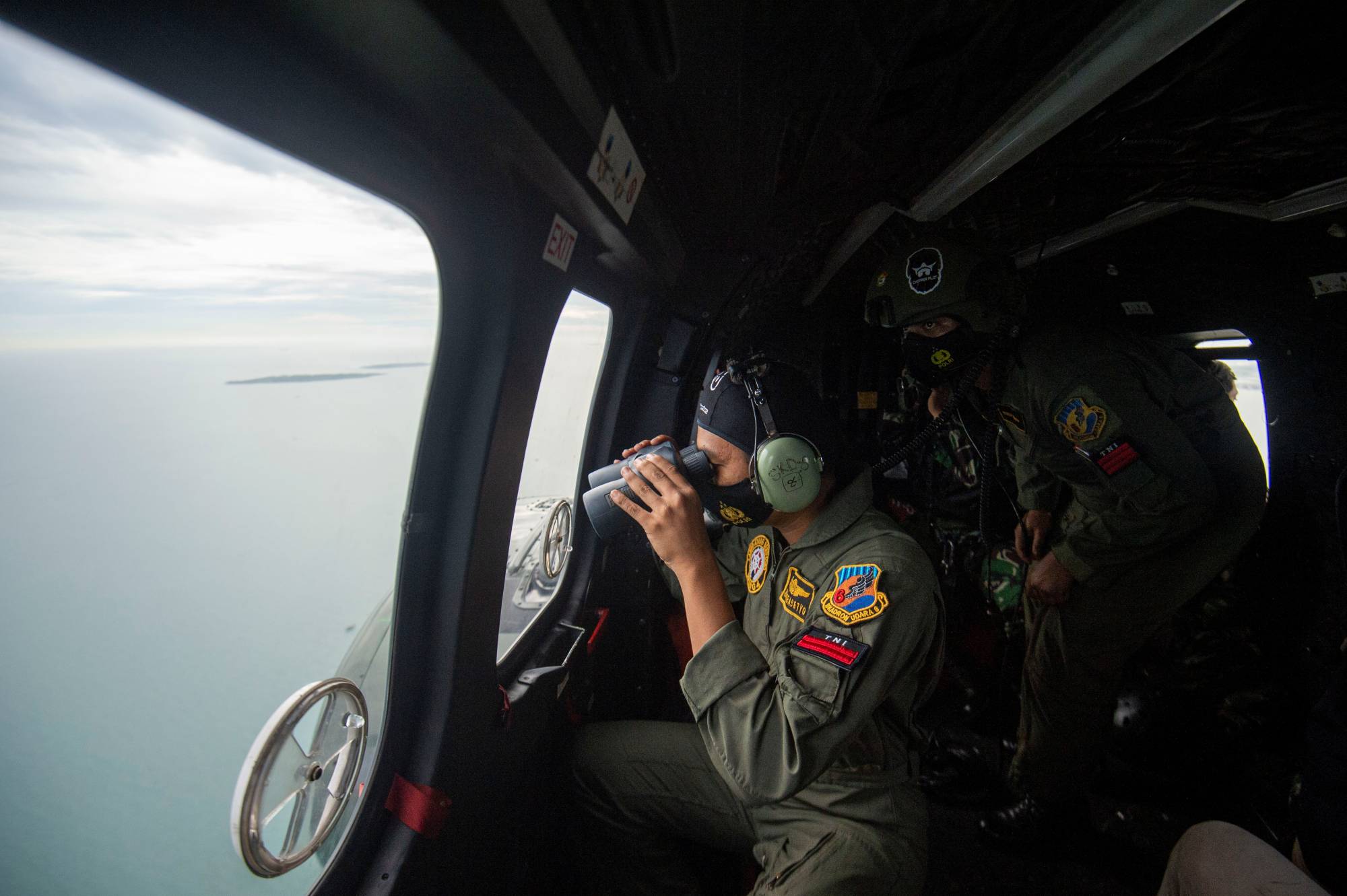 An Indonesian Air Force member looks through the window of a helicopter during an aerial search for the Sriwijaya Air SJ182, which crashed into the sea near Jakarta, on Sunday. | Antara Foto / via Reuters