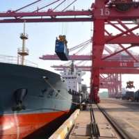 A container is loaded onto a cargo ship at a port in Lianyungang in China\'s eastern Jiangsu province on Thursday. Already the world’s top exporter, China’s shipments increased 3.6% in 2020, according to official data. | STR / VIA AFP-JIJI