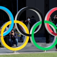 Visitors take photos with the Olympic rings in front of the Japan Olympics Museum in Tokyo on March 25, 2020, one day after the postponement of the 2020 Games. | REUTERS