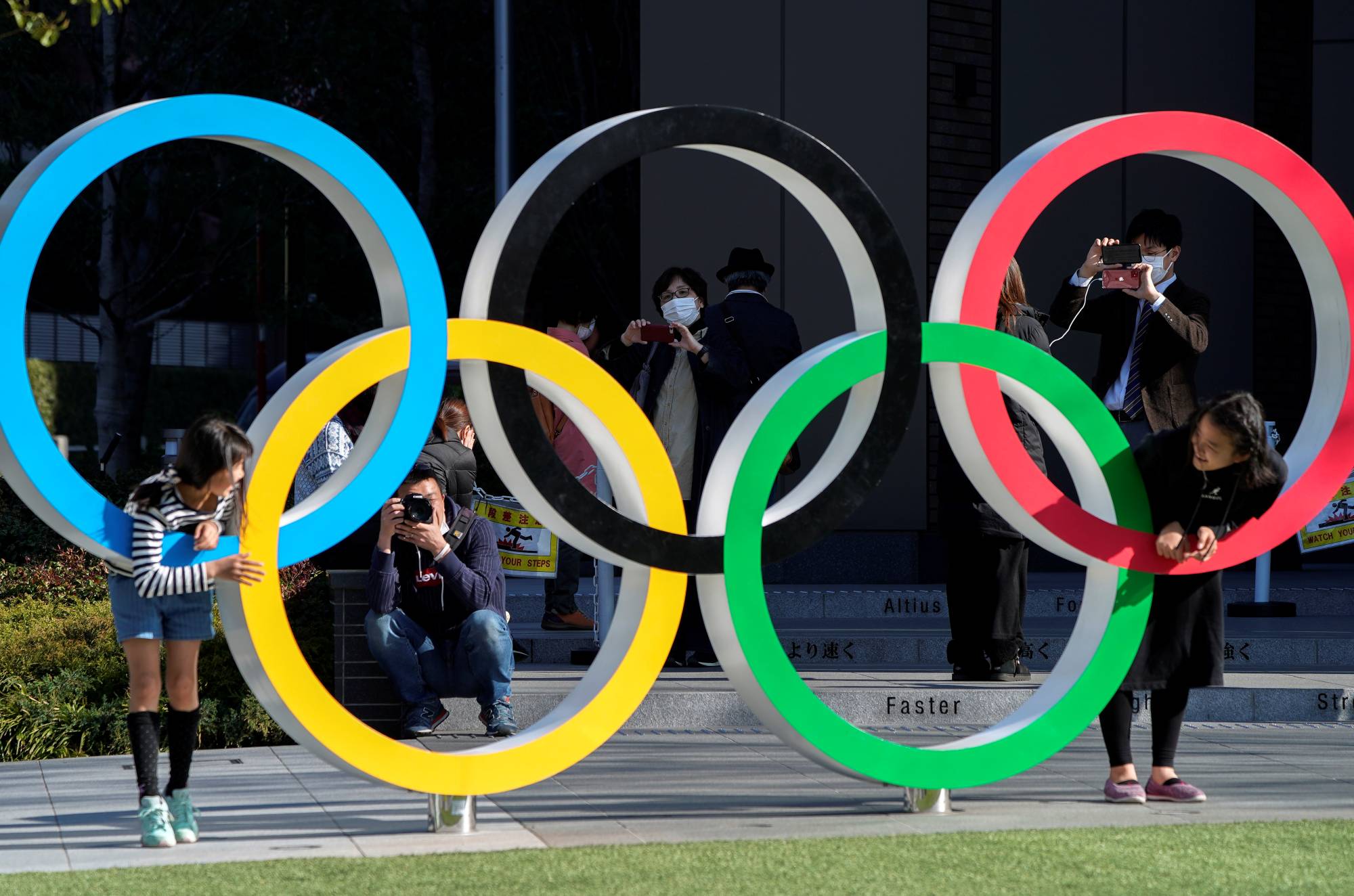 Visitors take photos with the Olympic rings in front of the Japan Olympics Museum in Tokyo on March 25, 2020, one day after the postponement of the 2020 Games. | REUTERS