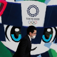A man wearing a mask walks past a poster featuring Tokyo 2020 mascot Miraitowa in Tokyo on June 4, 2020. | REUTERS
