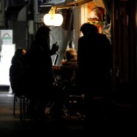 People drink by the table outside a bar that was staying open after 8 p.m., the time the government has asked restaurants and bars to close by, amid the coronavirus state of emergency in Tokyo on Friday. | REUTERS