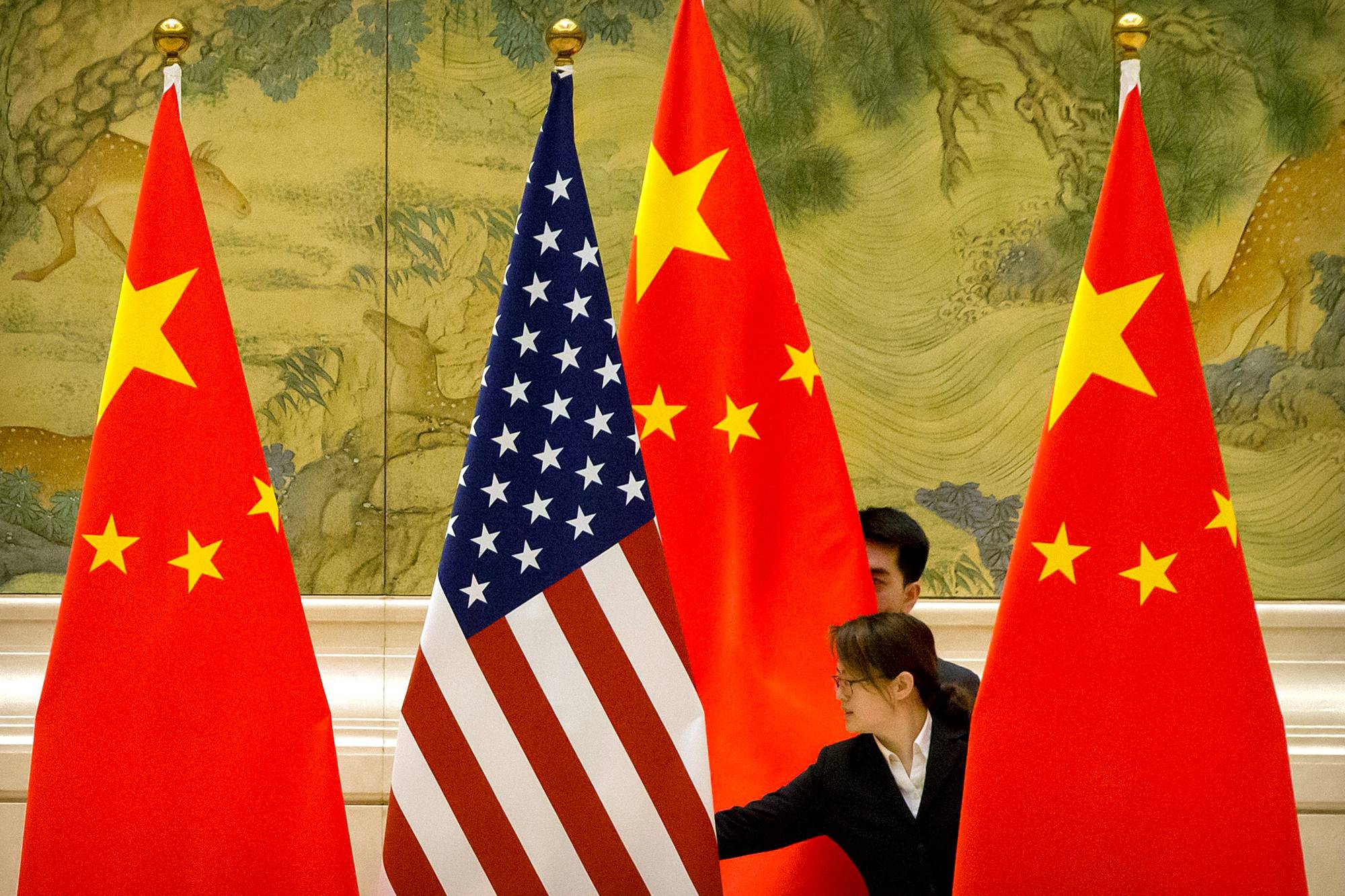 Chinese staffers adjust U.S. and Chinese flags before the opening session of Sino-U.S. trade negotiations in Beijing in February 2019. | POOL / VIA REUTERS