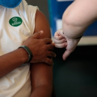 A health care worker receives a dose of a coronavirus vaccine in Sao Paulo on Sunday. The Japanese government may face a hard time convincing its people to get vaccinated amid skepticism against vaccines. | BLOOMBERG