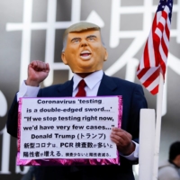 A man wearing a mask depicting U.S. President Donald Trump holds a placard in Toyko\'s Shibuya district on Jan. 9. | REUTERS
