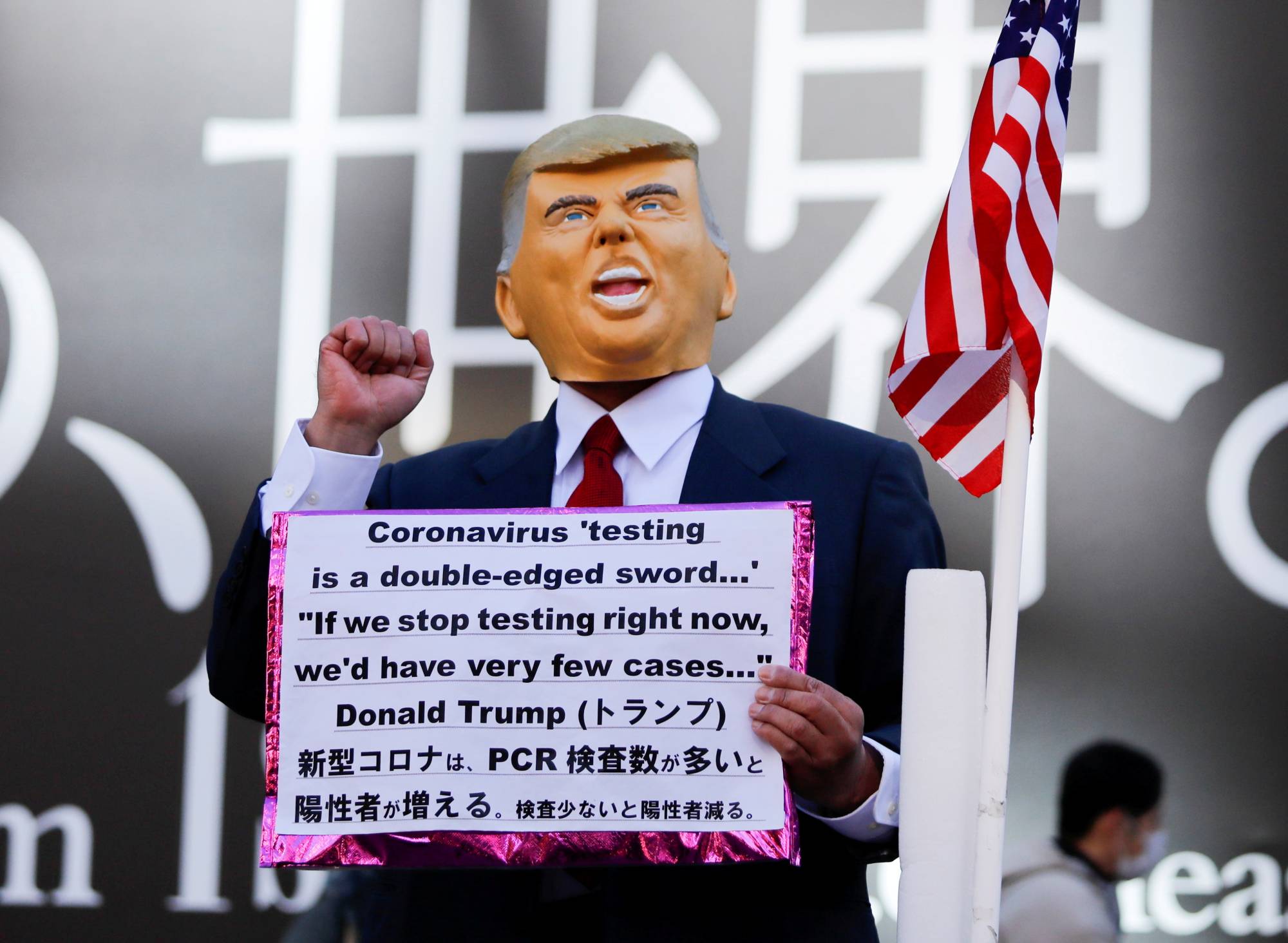 A man wearing a mask depicting U.S. President Donald Trump holds a placard in Toyko's Shibuya district on Jan. 9. | REUTERS