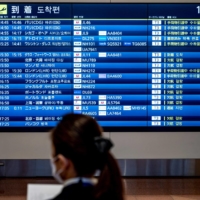 A staff member stands in front of a board displaying information on flight arrivals and cancellations at Tokyo\'s Haneda Airport on Dec. 27. | AFP-JIJI