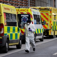 A medical delivery driver wearing PPE runs along a line of parked ambulances outside the Royal London hospital in London on Tuesday. An estimated 12% of people in England had been infected with the novel coronavirus by December last year, up from 9% in November, according to official antibody data released Tuesday. Health chiefs have warned intensive care units risk being overwhelmed by the surge in cases that has already led to the country suffering record numbers of daily deaths. | AFP-JIJI