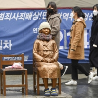 Passersby look at a statue symbolizing the so-called comfort women, who suffered under Japan’s military brothel system before and during World War II, in front of the Japanese Embassy in Seoul on Friday. | KYODO