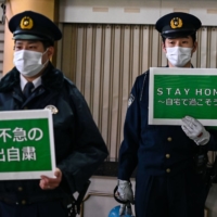 Policemen hold signs asking people to stay home amid rising numbers of coronavirus cases in Tokyo on Friday. | AFP-JIJI 