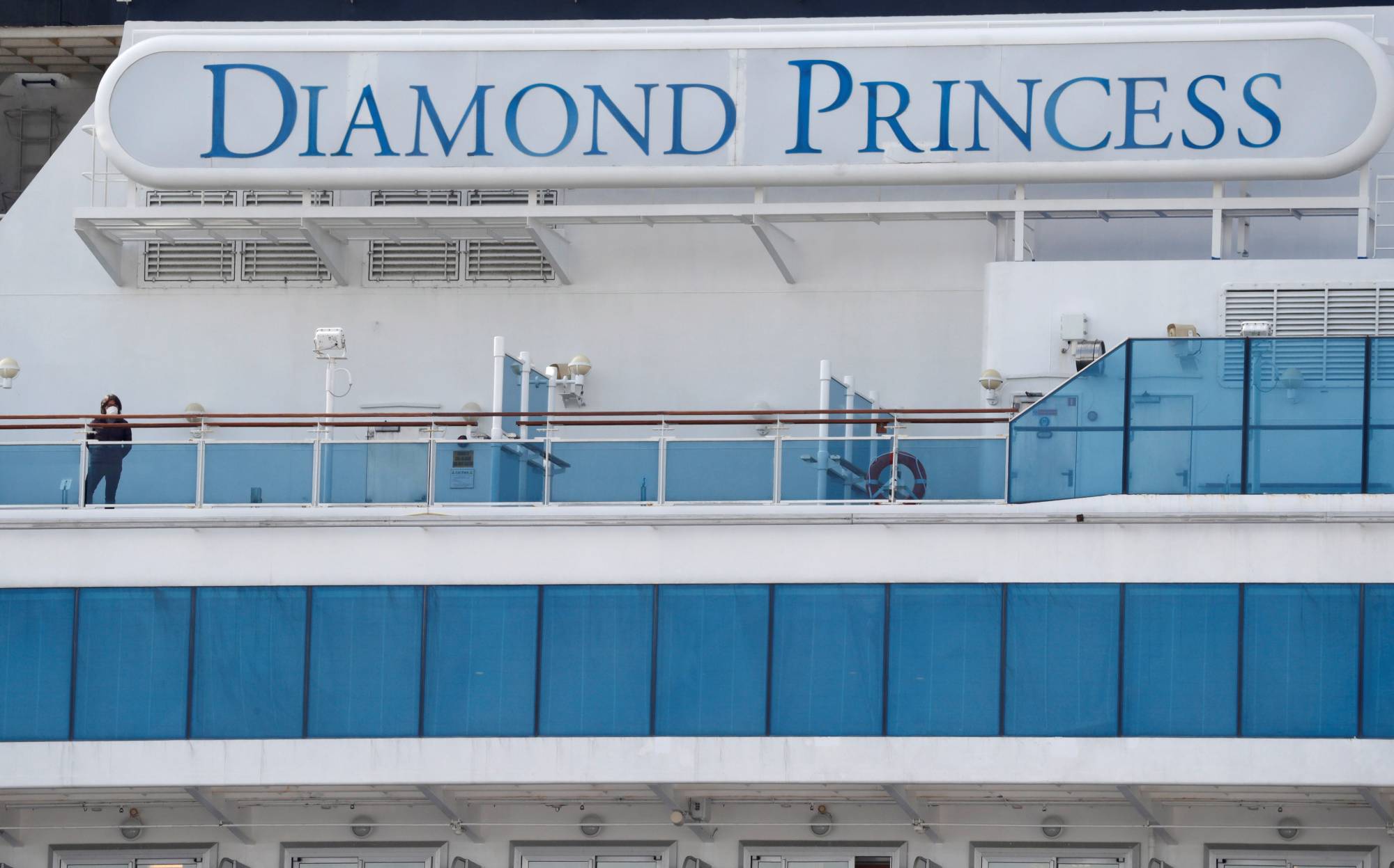 Masked passengers look out from the Diamond Princess cruise ship docked at Yokohama Port in February 2020. | REUTERS