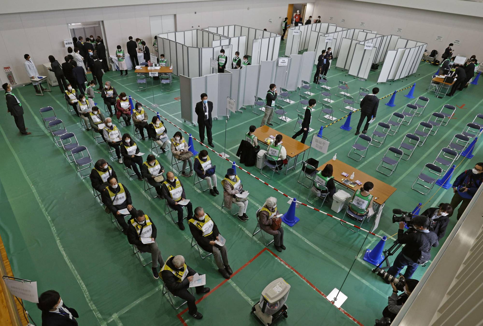 Social distancing measures are taken, with partitions set up to separate participants, during a coronavirus vaccination simulation held at a university gymnasium in Kawasaki on Wednesday. | KYODO