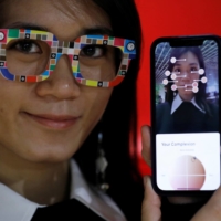 An employee of online fashion retailer Zozo Inc. poses with \"Zozoglass\" and its smartphone application, used to measure skin tone for ordering cosmetics online, during a demonstration at the company\'s office in Tokyo on Thursday. | REUTERS