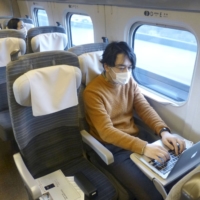 A man works remotely in a Tohoku shinkansen carriage converted into an office space in a trial held Monday. | KYODO