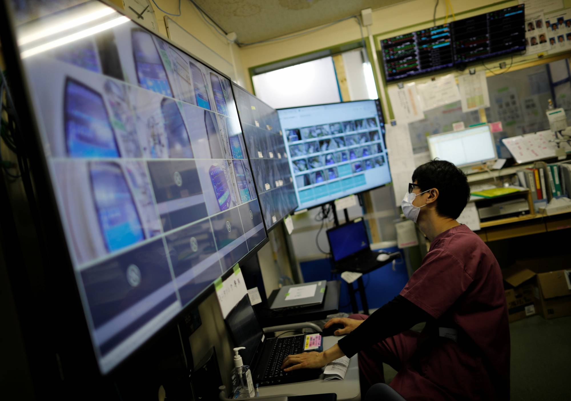 A medical worker monitors remotely live footage of COVID-19 patients in the intensive care unit at St. Marianna Medical University Hospital in Kawasaki in May. Less efficient use of hospital beds in Japan is causing a strain on its health care system amid the pandemic. | REUTERS