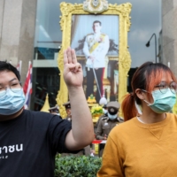 A protest leader, Parit \"Penguin” Chiwarak, flashes a three-finger salute next to a picture of Thailand\'s King Maha Vajiralongkorn during a protest in Bangkok demanding the resignation of Prime Minister Prayut Chan-ocha, on Jan. 25.  | REUTERS
