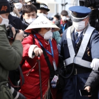 A police officer escorts a passenger away from the media as she disembarks from the Diamond Princess cruise ship in Yokohama on Feb. 19, 2020. | REUTERS