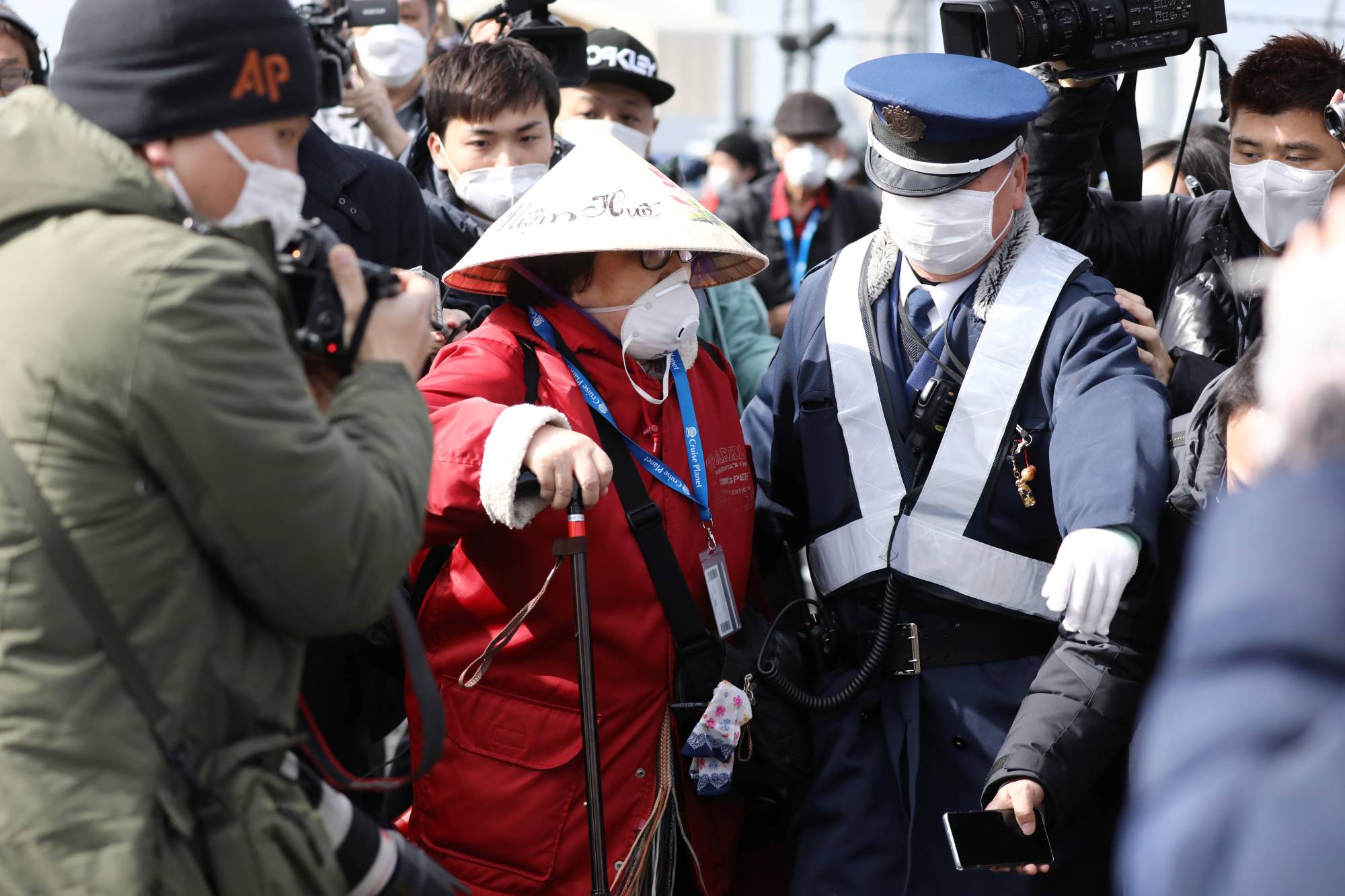 A police officer escorts a passenger away from the media as she disembarks from the Diamond Princess cruise ship in Yokohama on Feb. 19, 2020. | REUTERS