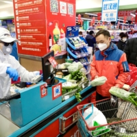 A worker in protective suit serves customers at a supermarket following the outbreak of the novel coronavirus in Wuhan, China, in February last year.  | CHINA DAILY / VIA REUTERS
