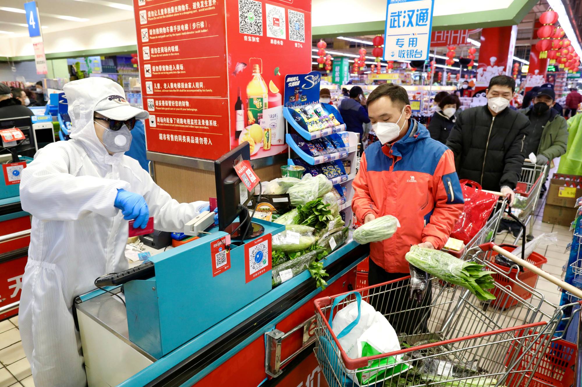 A worker in protective suit serves customers at a supermarket following the outbreak of the novel coronavirus in Wuhan, China, in February last year. | China Daily / via REUTERS