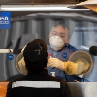A health care worker collects a sample from a visitor at a temporary COVID-19 testing station in Seoul, on Jan. 19.   | BLOOMBERG