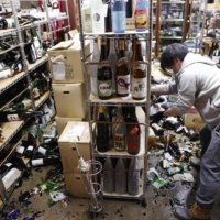 The manager of a liquor store cleans up broken bottles in the city of Fukushima following a strong earthquake. | KYODO