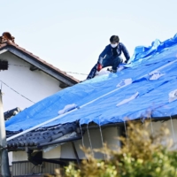 Men cover the damaged roof of a house with a blue sheet in Shinchi, Fukushima Prefecture, on Sunday. | KYODO