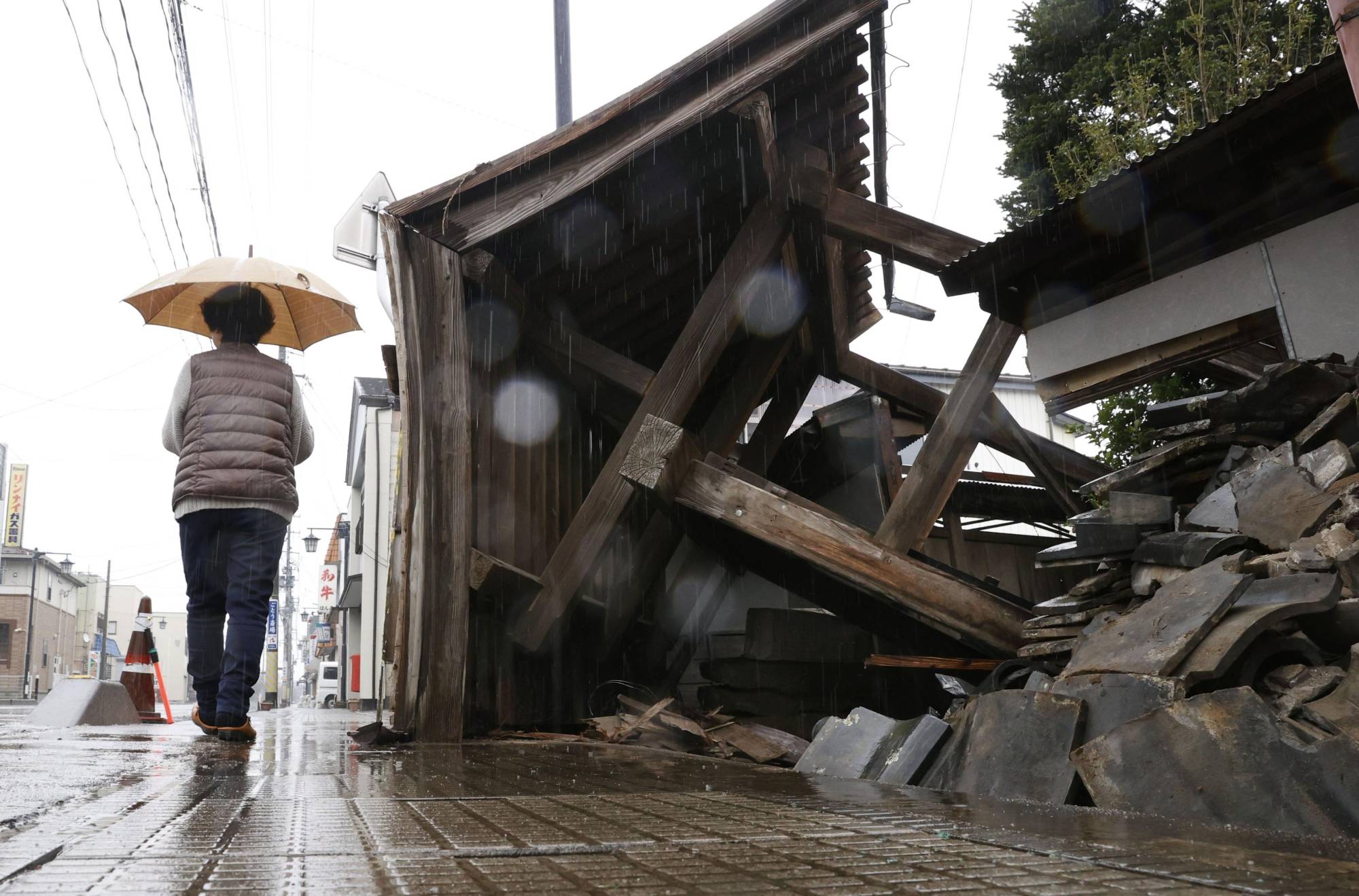 A woman walks past a damaged gate in the town of Kori, Fukushima Prefecture, in the rain on Monday. | KYODO