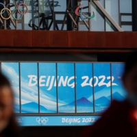 People wearing face masks walk near the office complex of the Beijing Organising Committee for the 2022 Winter Games, a year ahead of the opening of the Olympics in Beijing on Feb. 4. | REUTERS
