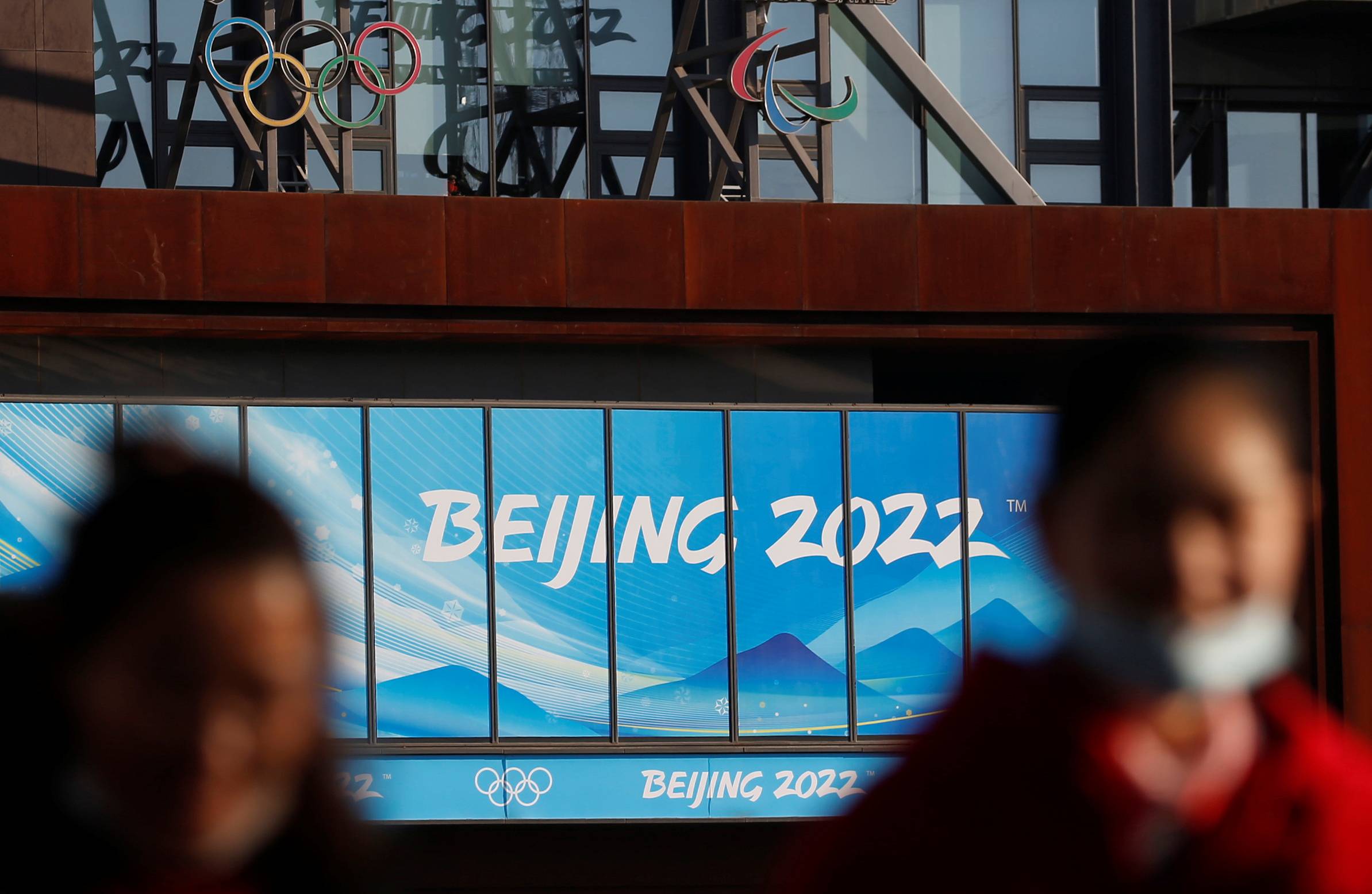 People wearing face masks walk near the office complex of the Beijing Organising Committee for the 2022 Winter Games, a year ahead of the opening of the Olympics in Beijing on Feb. 4. | REUTERS