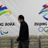 A man walks past a board with logos of 2022 Winter Olympic Games at a souvenir shop under renovation in Beijing on Jan. 29. | REUTERS