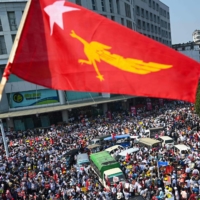 A protester waves the National League for Democracy (NLD) flag while others take part in a demonstration in Yangon on Monday against the military coup. | AFP-JIJI