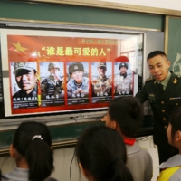 A paramilitary police officer talks next to a screen showing frontier soldiers of the People\'s Liberation Army during an event to educate students about national defense at a primary school in Wuzhishan, China, on Tuesday.  | CHINA DAILY / VIA REUTERS