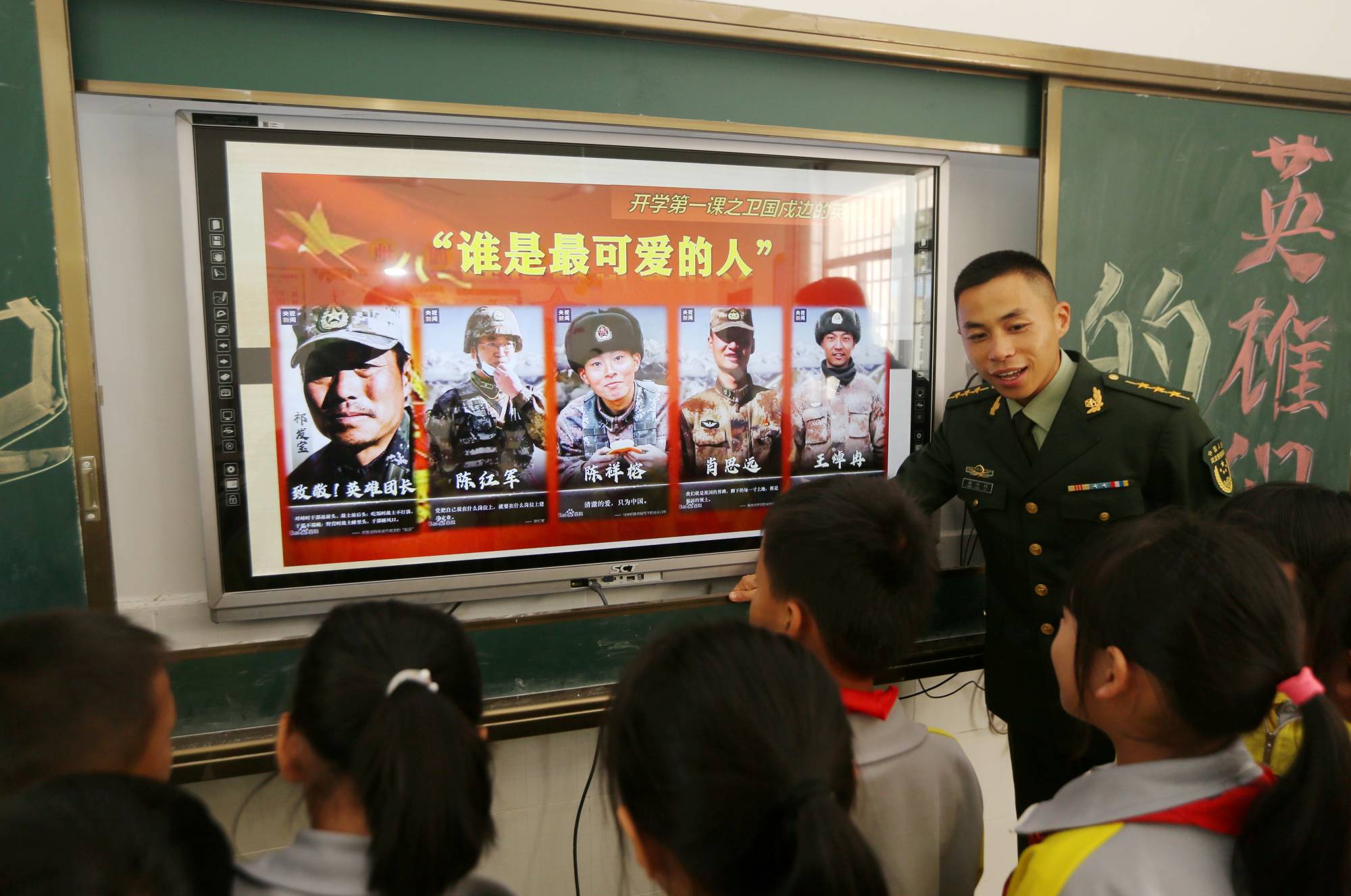 A paramilitary police officer talks next to a screen showing frontier soldiers of the People's Liberation Army during an event to educate students about national defense at a primary school in Wuzhishan, China, on Tuesday.  | CHINA DAILY / VIA REUTERS