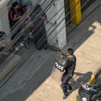 A policeman points his weapon at people in Taunggyi, Myanmar, on Sunday as security forces continue to crackdown on demonstrations by protesters against the military coup. | AFP-JIJI