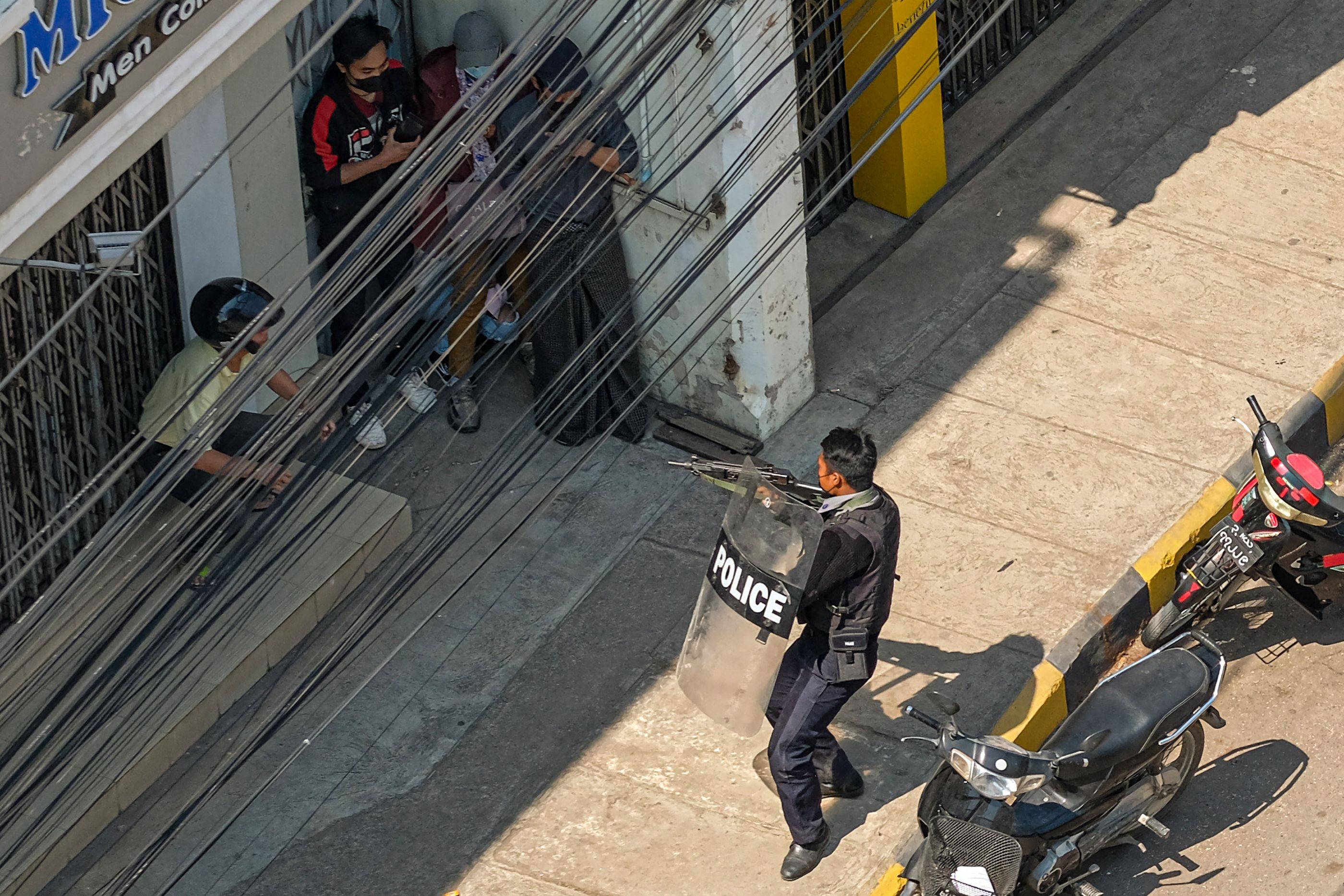 A policeman points his weapon at people in Taunggyi, Myanmar, on Sunday as security forces continue to crackdown on demonstrations by protesters against the military coup. | AFP-JIJI